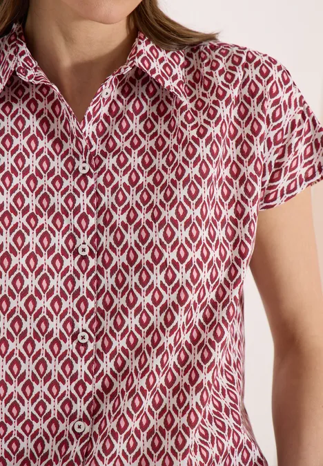 Eine Frau trägt eine kurzärmlige Bluse mit rot-weißem, geometrischem Muster.